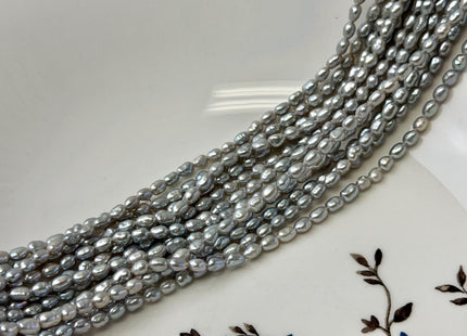 May include: Strands of gray freshwater pearls. The pearls are oval-shaped and have a lustrous sheen. The pearls are displayed on a white plate with a floral design.