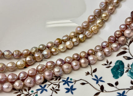 May include: Three strands of lustrous, irregularly shaped pearls in shades of pink, gold, and cream. The pearls are strung together, creating a necklace or bracelet. The background is a white plate with a floral design.